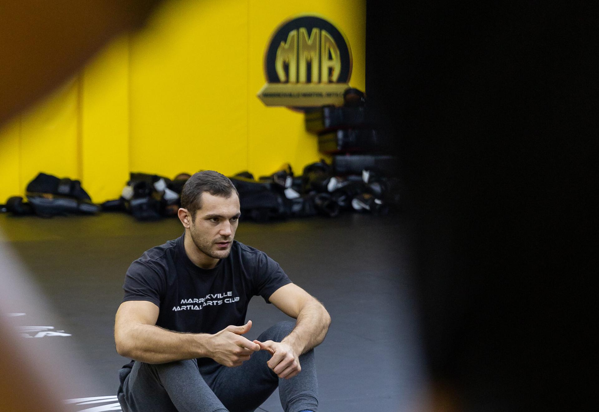 Coach on the mats beneath the MMAC logo